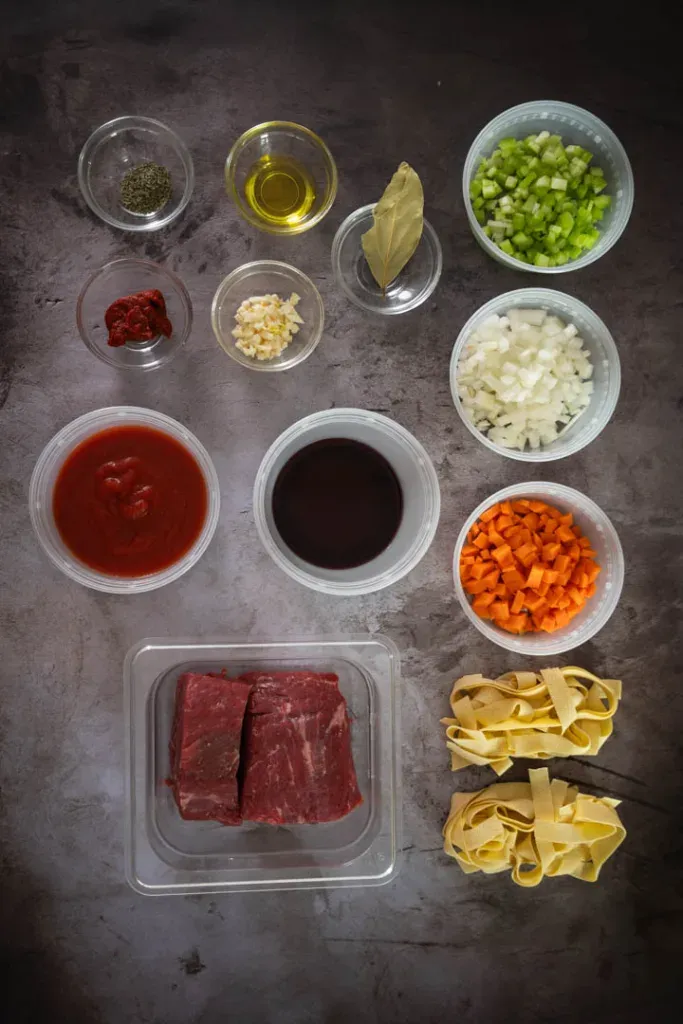 All ingredients for beef ragu pappardelle laid out including beef, aromatics, tomatoes, wine, and pasta