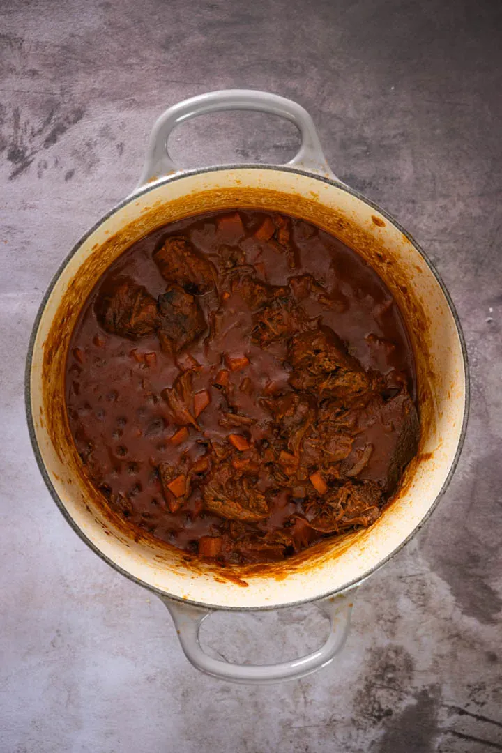 Beef ragu slowly simmering in a Dutch oven with rich tomato sauce and tender meat