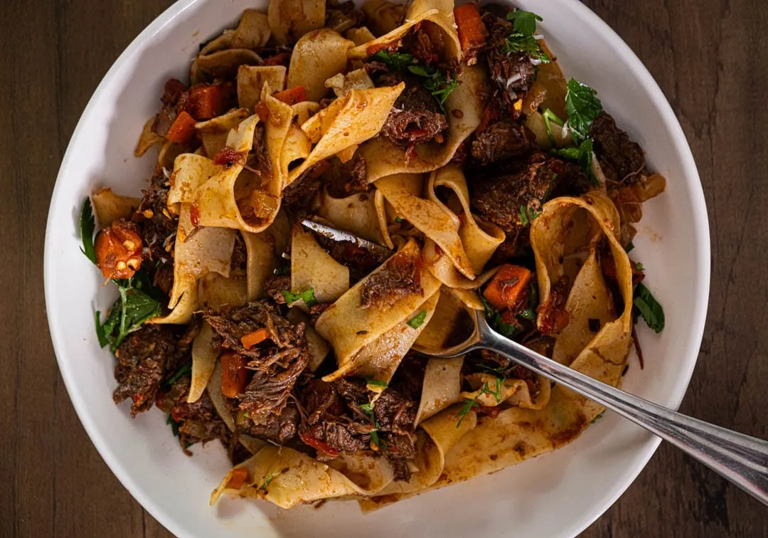 Glossy pappardelle ribbons tangled in deep mahogany beef ragu with wisps of steam and a snow-drift of freshly grated Parmesan