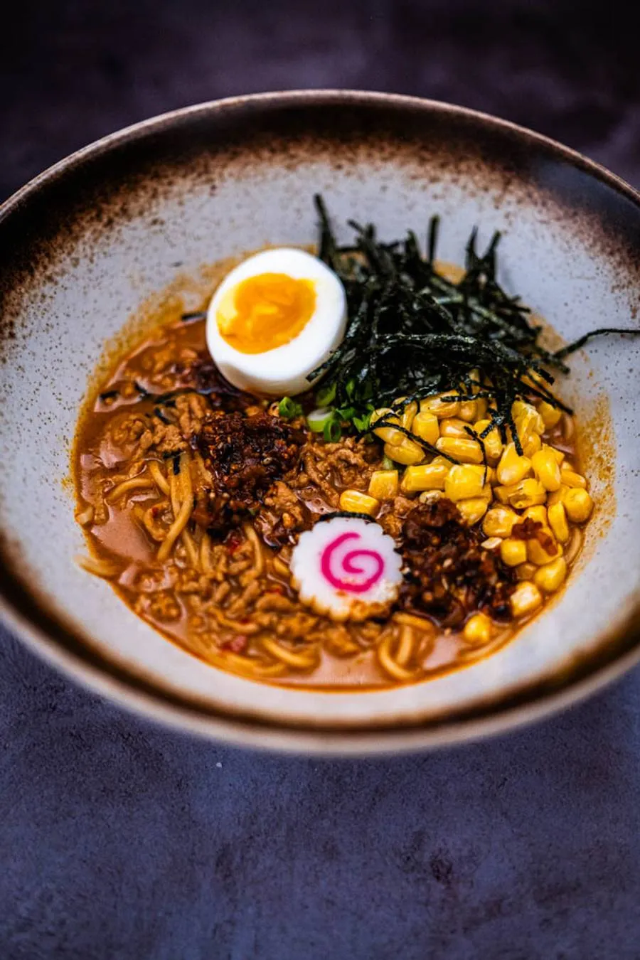 Two bowls of bold spicy miso ramen from above, steam rising, garnished with scallions, nori, and a pool of garlic-togarashi oil on each