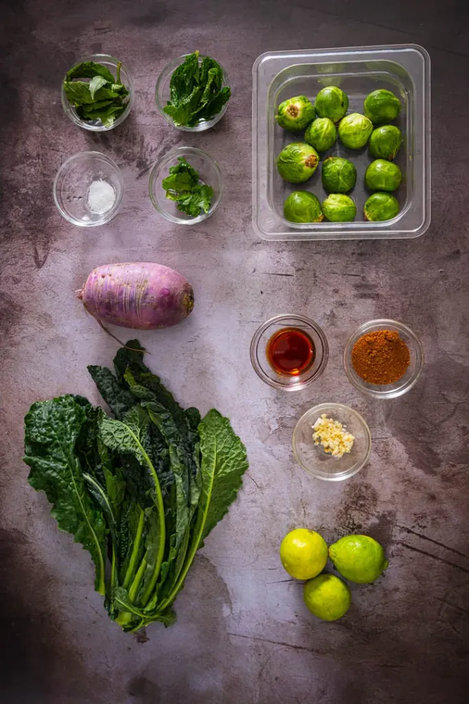 Fresh ingredients for Brussels sprouts salad including Brussels sprouts, kale, herbs, lime, and garlic