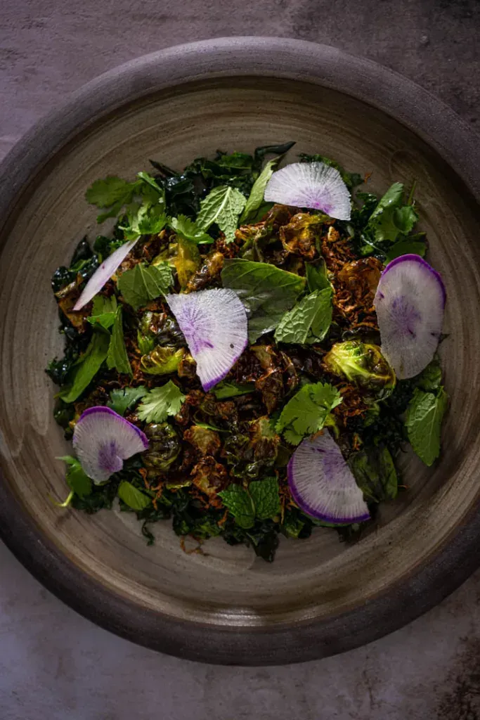 Dramatic mound of dressed kale and shaved sprouts crowned with shatteringly crisp fried Brussels sprout leaves