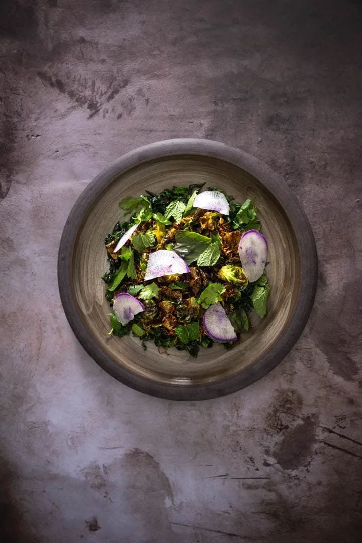 Brussels sprouts salad with crispy fried leaves, shaved kale, fresh herbs, and purple daikon on a white plate