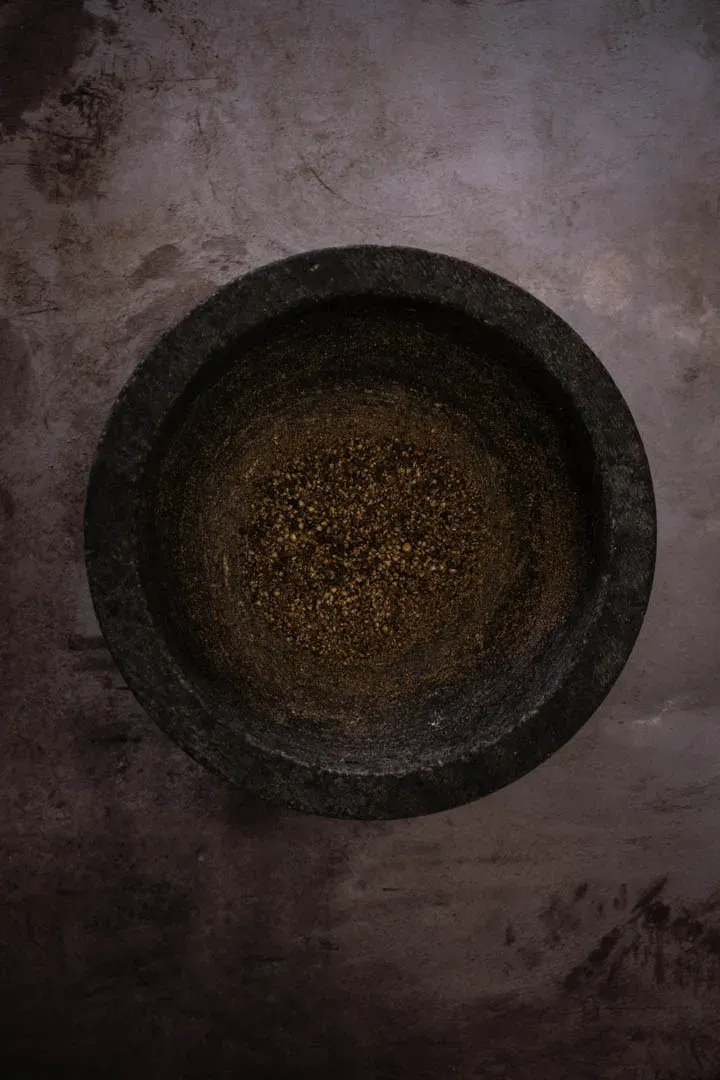 Toasted black peppercorns being ground in a mortar and pestle for authentic cacio e pepe