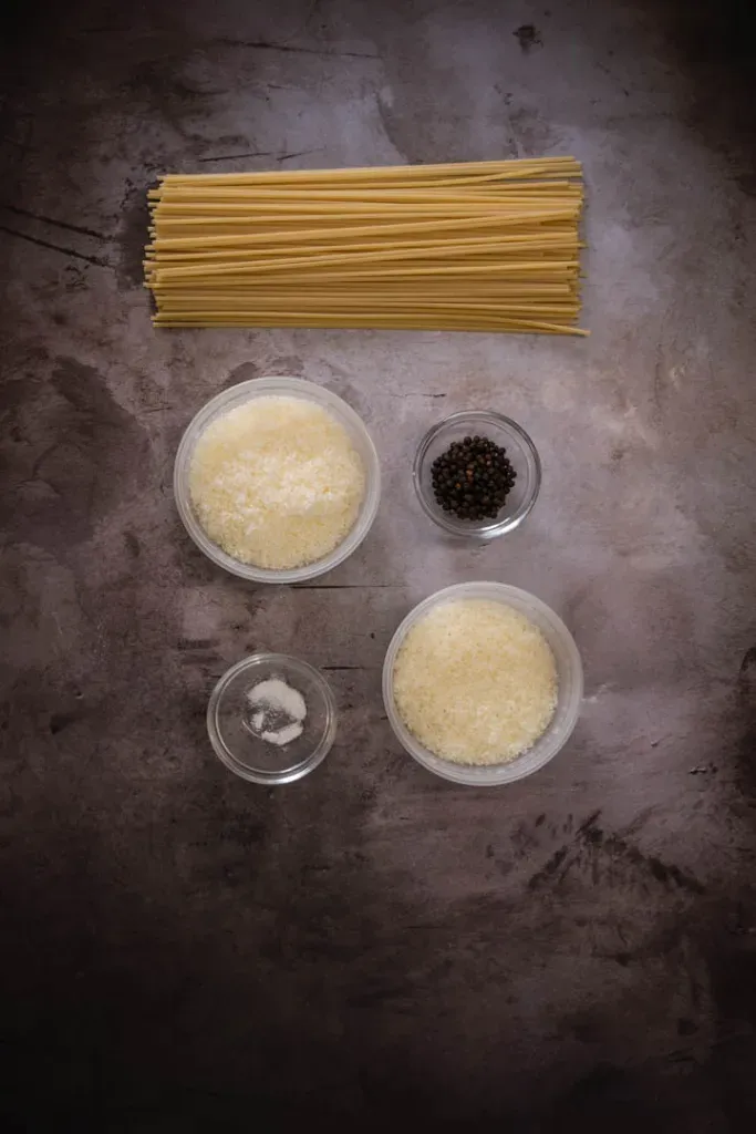 Fresh ingredients for cacio e pepe: spaghetti, Pecorino Romano cheese, and whole black peppercorns