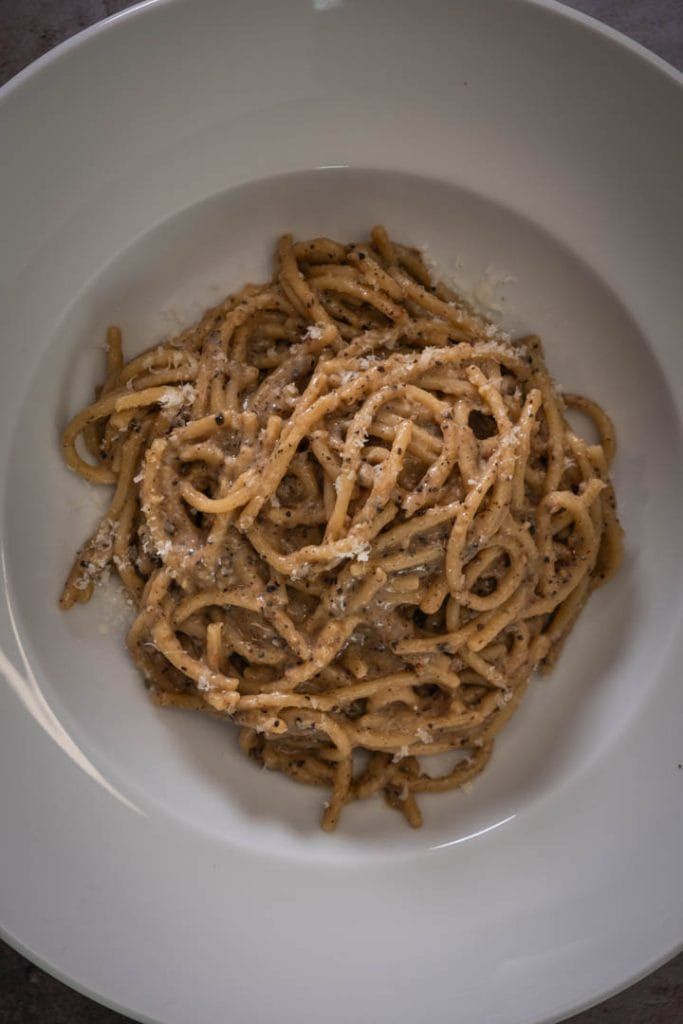Plated cacio e pepe garnished with freshly cracked black pepper and grated Pecorino Romano