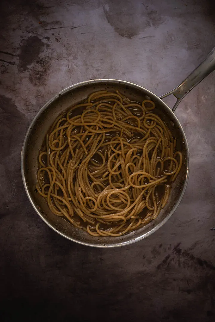 Spaghetti being tossed with toasted pepper and starchy pasta water in a hot pan