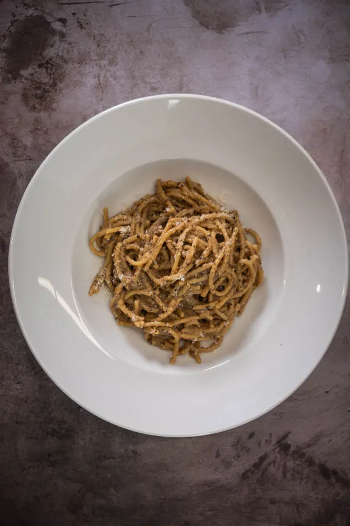 Tight twirl of spaghetti cacio e pepe glistening with velvety Pecorino sauce, flecked with coarsely cracked black pepper on a dark plate