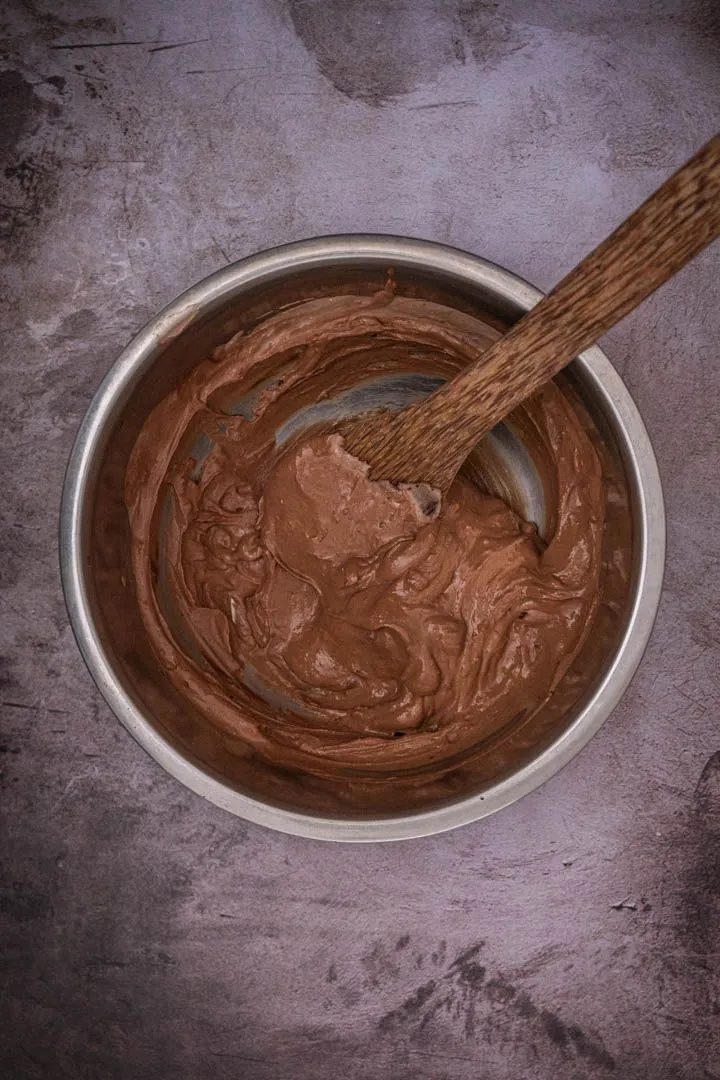 Chocolate tofu pudding being strained through a fine-mesh sieve into a bowl, melted chocolate beside it