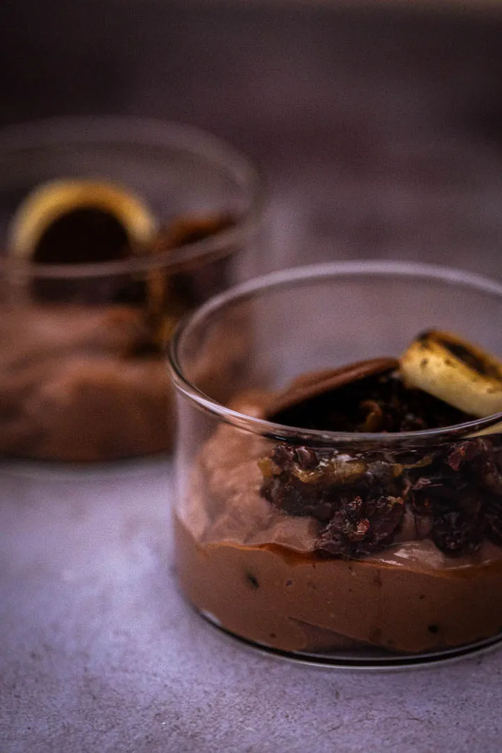 Assembled chocolate tofu pudding bowl with candied cacao nibs and banana slices, olive oil drizzle visible