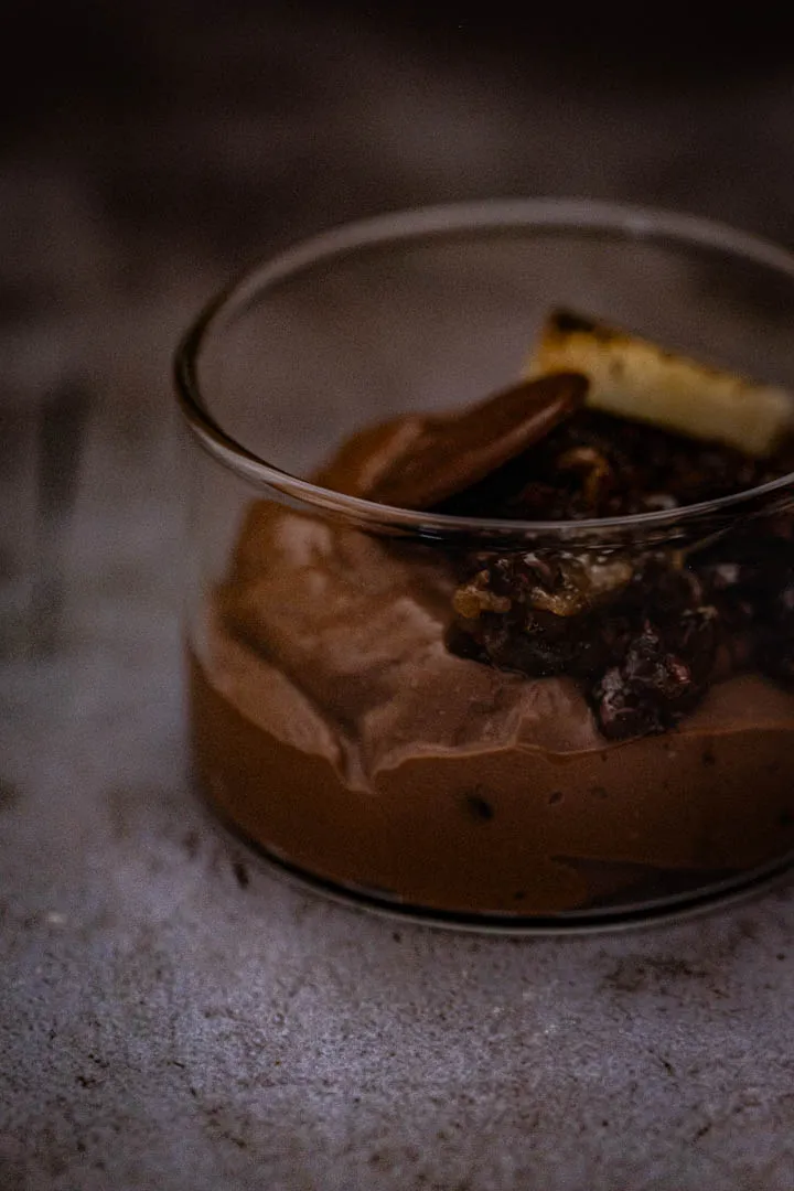 Silky chocolate tofu pudding in a shallow bowl topped with candied cacao nibs, sliced banana, and a drizzle of olive oil