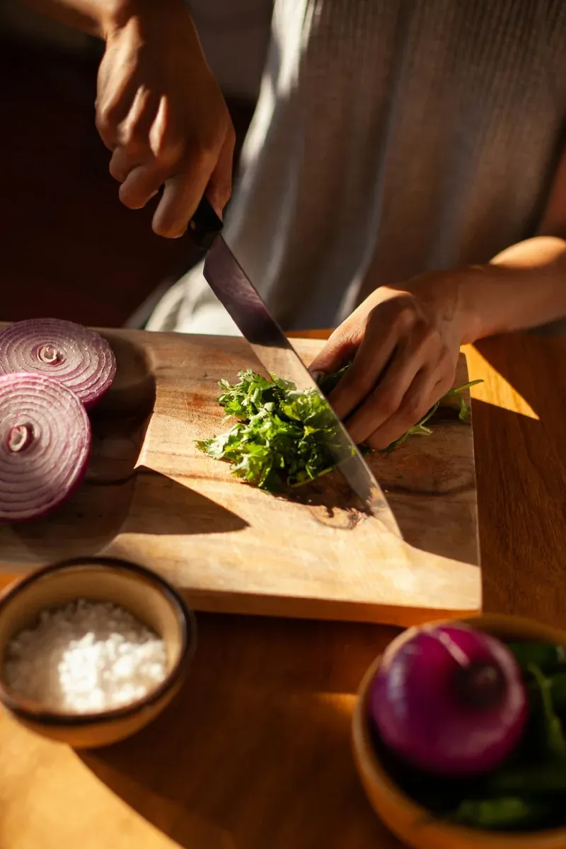 Close-up of a sharp chef's knife on a wooden cutting board with freshly chopped herbs