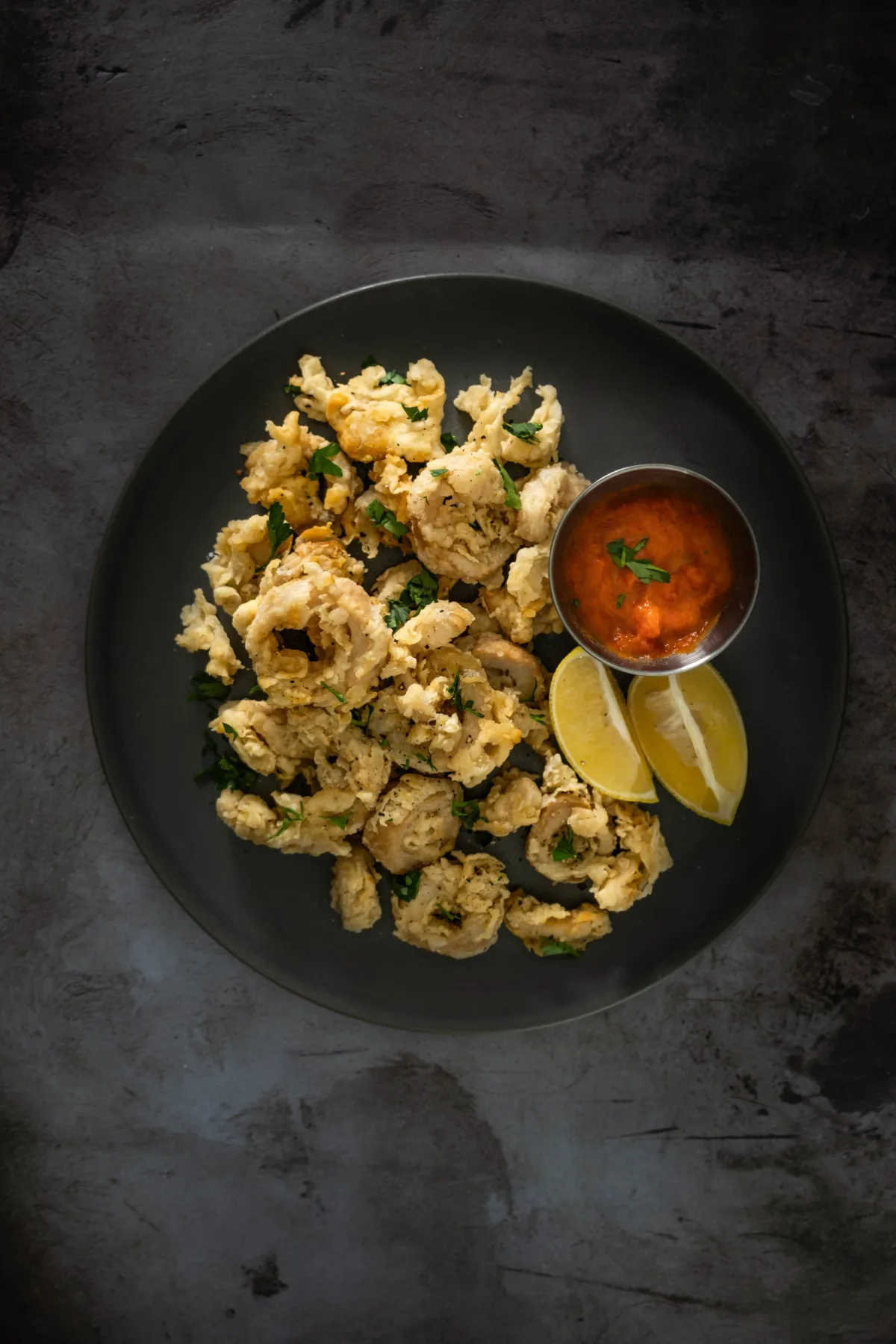 Golden crispy vegan calamari rings made from king oyster mushrooms served with lemon wedges on a plate