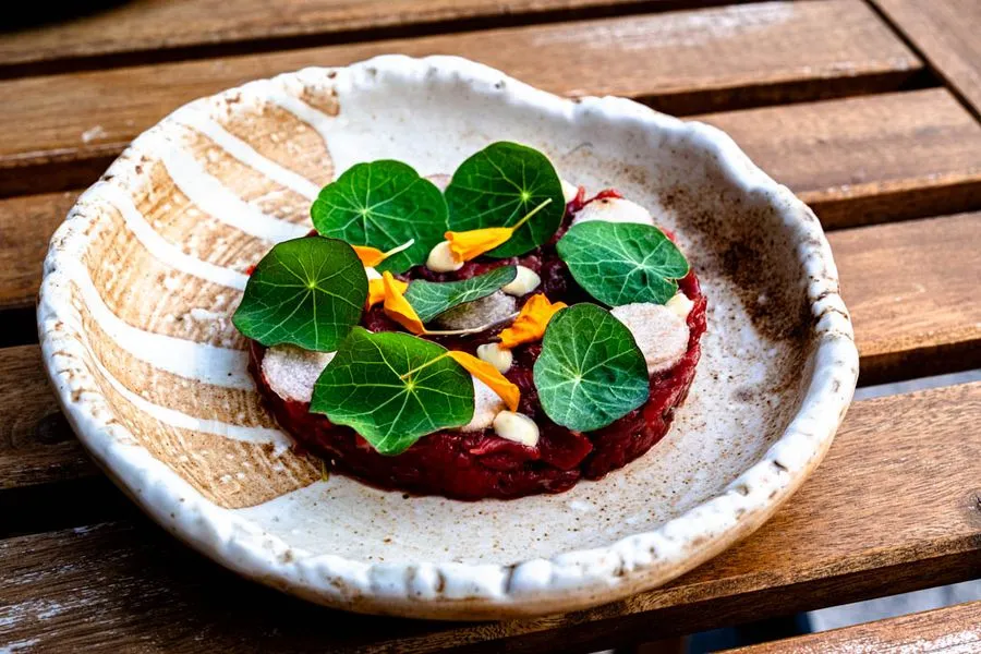 Yukhwe beef tartare at Giwa Verdun, a Korean-style tartare with pear, sesame, soy, egg yolk, and nasturtium on a dark ceramic plate