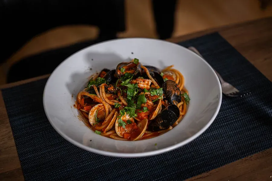 Glossy gochujang-kimchi seafood bucatini with open mussels and pink shrimp in a wide bowl, the fiery red sauce clinging to every strand