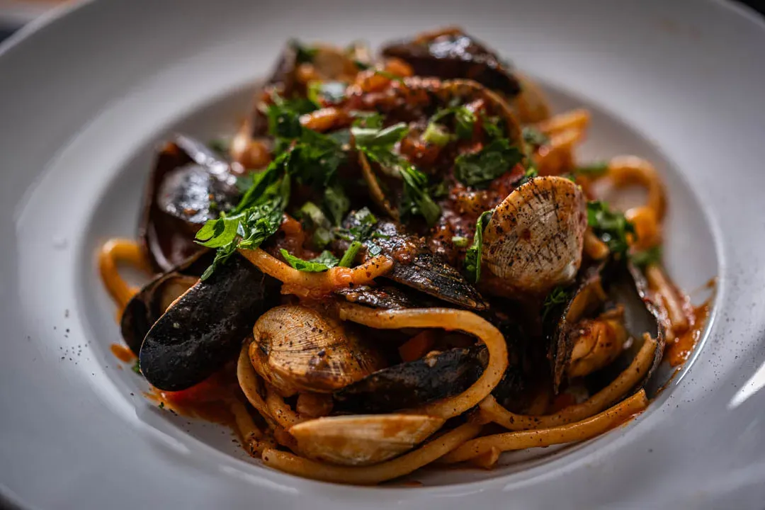 Tangle of glossy bucatini coated in fiery red gochujang-kimchi sauce with open mussels, pink shrimp, and seared scallops nestled on top