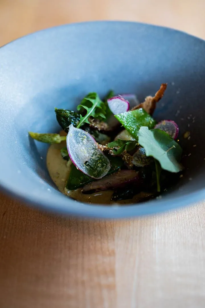 Green asparagus and snap peas with pistachio and vibrant microgreens plated elegantly at Hoogan et Beaufort Montreal