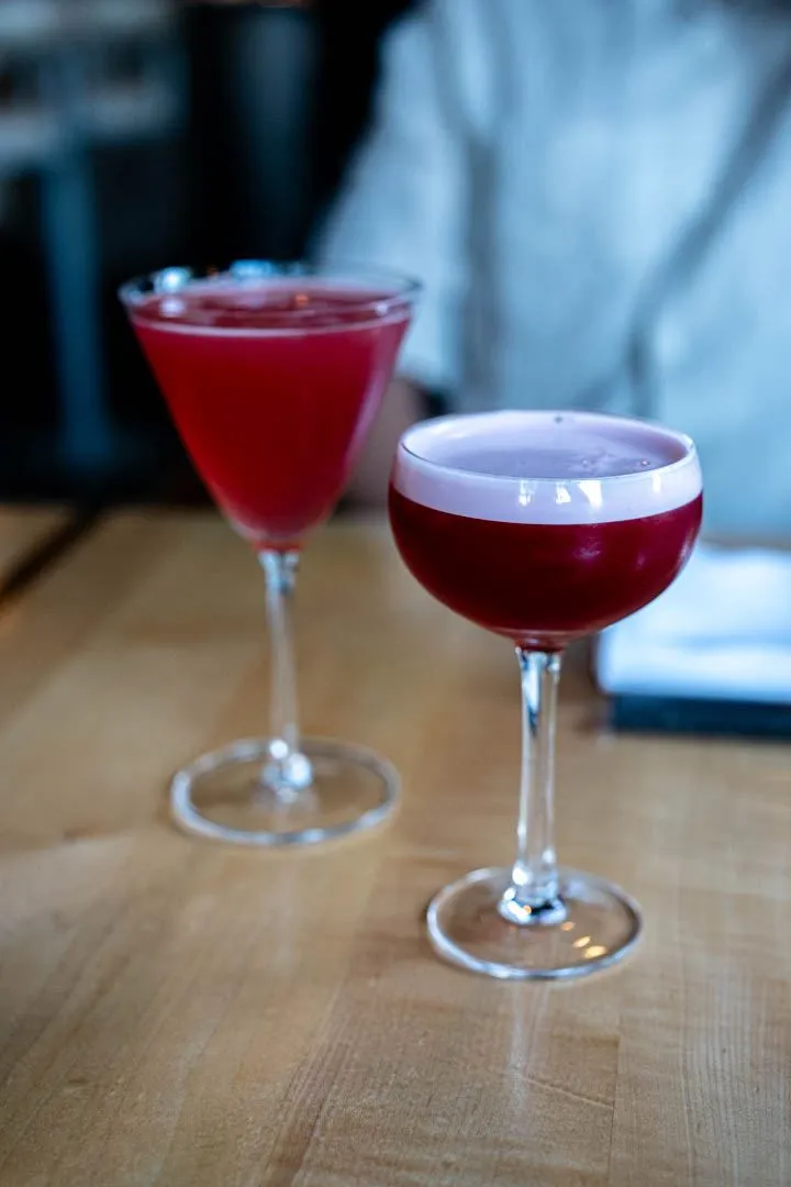 Elegant cocktails at Hoogan et Beaufort Montreal, two glasses with citrus garnish on a marble bar, softly lit in the warm restaurant atmosphere