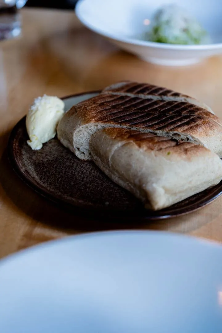 Grilled focaccia with whipped butter at Hoogan et Beaufort Montreal, sliced bread on a wooden board with a small ramekin of pale whipped butter