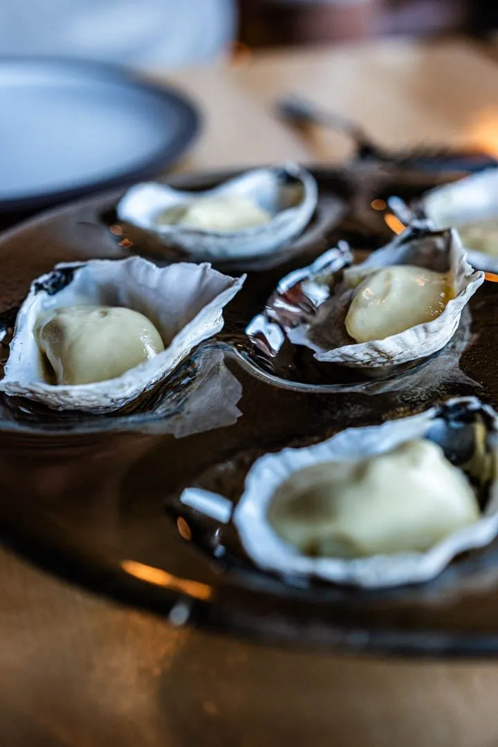 Hot oysters with cider sabayon served on a bed of sea salt at Hoogan et Beaufort Montreal, the shells glistening under warm restaurant lighting