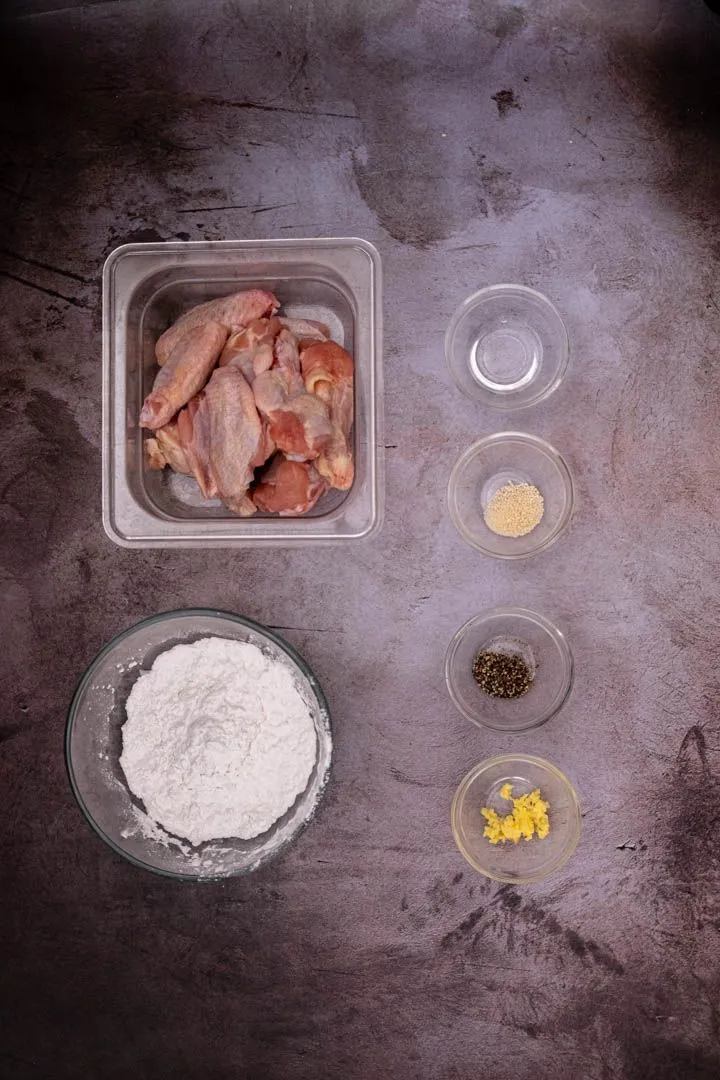 Vietnamese fish sauce wing ingredients on a counter: chicken wings, potato starch, fish sauce, sugar, lime, Thai chilies, garlic, and fresh ginger