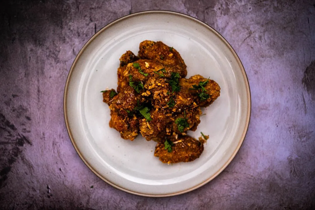 Golden-lacquered Vietnamese fish sauce wings glistening with sticky caramel glaze, piled on a plate and crowned with crispy fried garlic and fresh cilantro