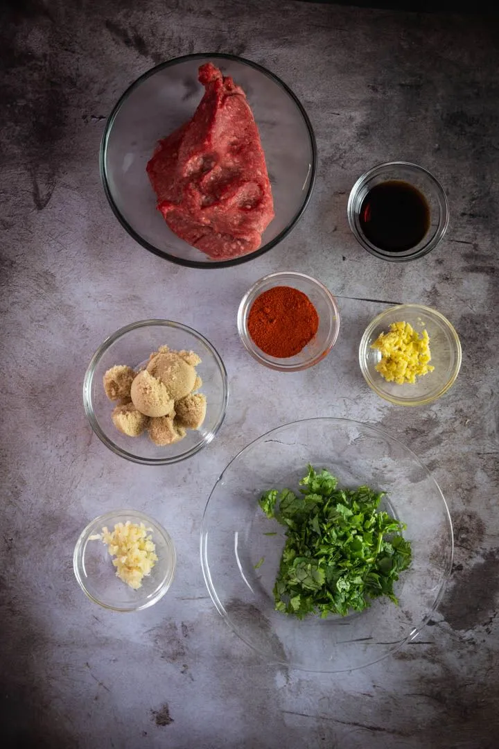 Ingredients for lamb meatballs laid out on a counter: kabocha squash, ground lamb, fresh herbs, gochujang, hoisin, peanuts, and spices