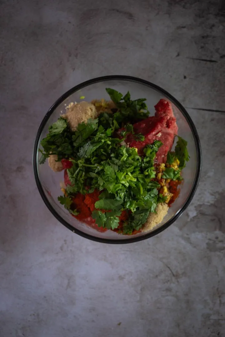 Ground lamb mixed with brown sugar, garlic, ginger, fresh mint, cilantro, and gochugaru in a stainless steel bowl