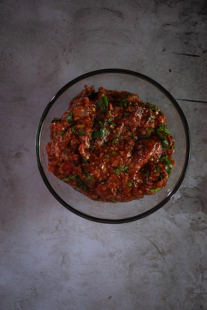 Lamb meatballs formed and arranged on a surface, ready to be pan-seared in a hot skillet