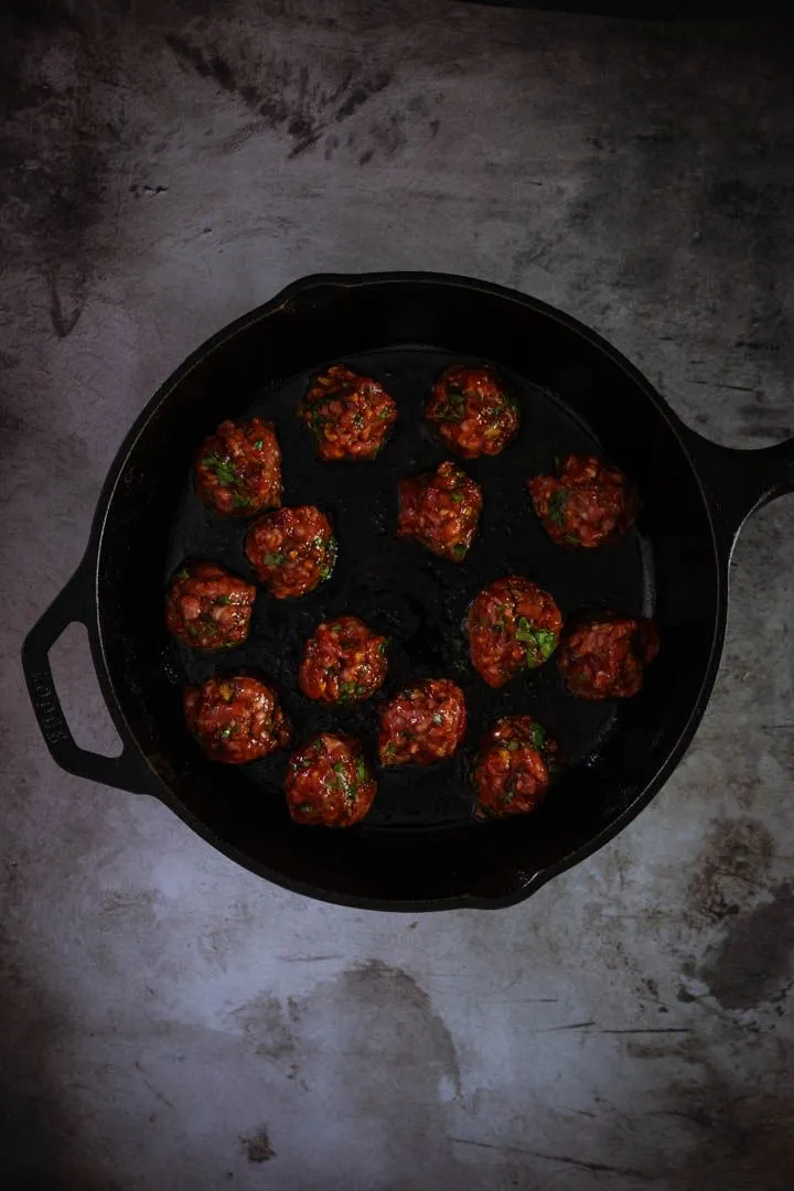 Seared lamb meatballs resting in a skillet with deep golden-brown crust on all sides