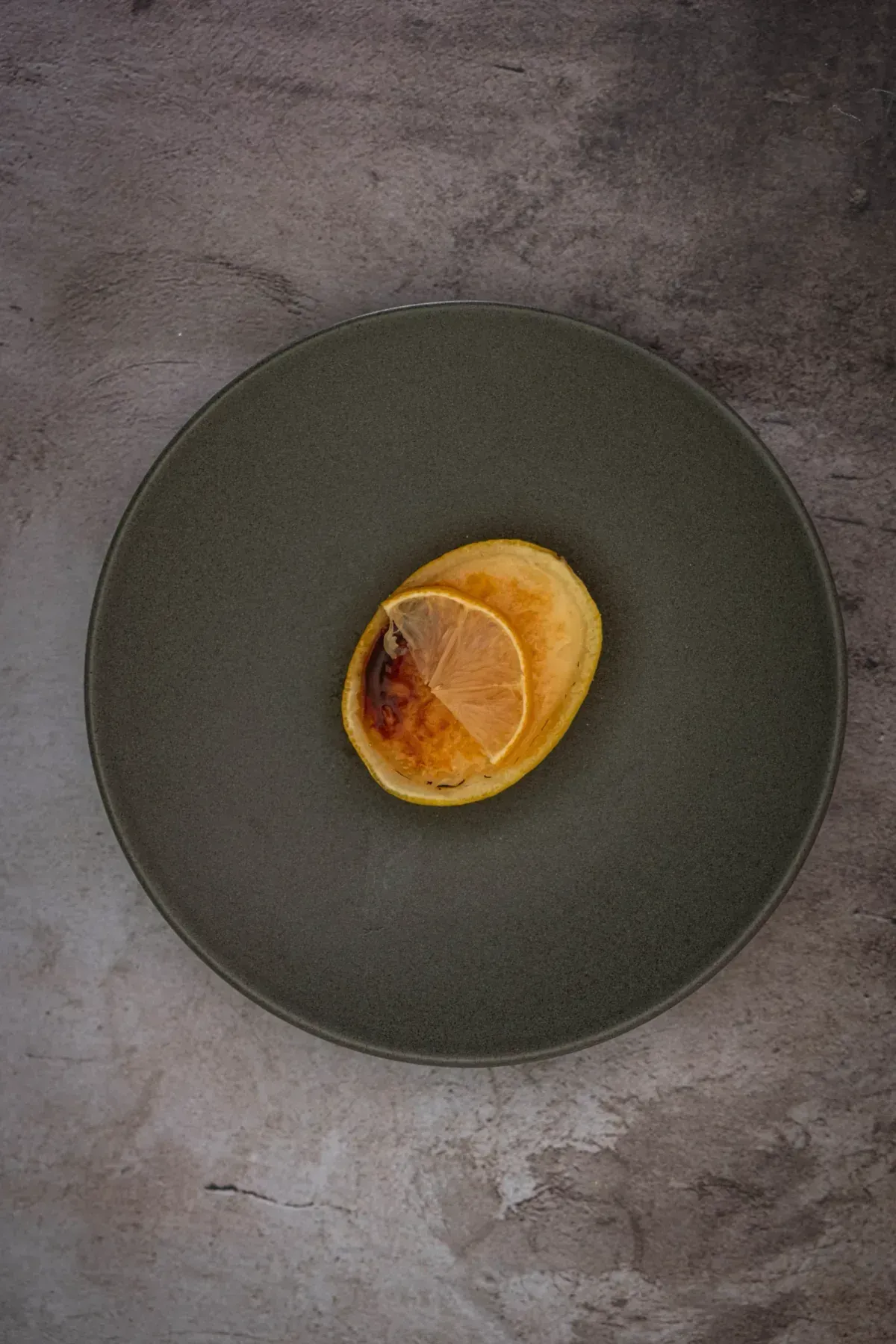 Silky lemon posset brulee nestled in hollowed lemon shells, each topped with a glassy amber caramelized sugar crust catching the light