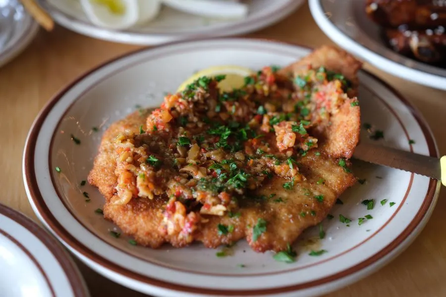 Golden bomba schnitzel with crunchy breading, spicy bomba sauce and fresh herbs on a white plate at McKiernan Montreal
