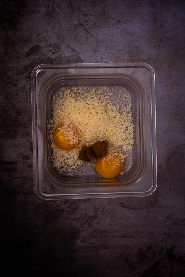 Egg yolks, grated Parmesan, and miso paste sitting together in a glass container before whisking