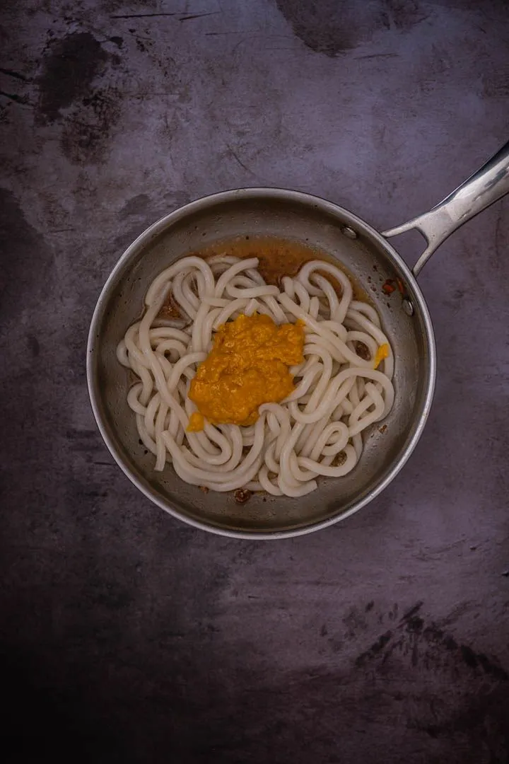 Udon noodles in a pan with the golden yolk-cheese-miso sauce dolloped on top, about to be tossed together