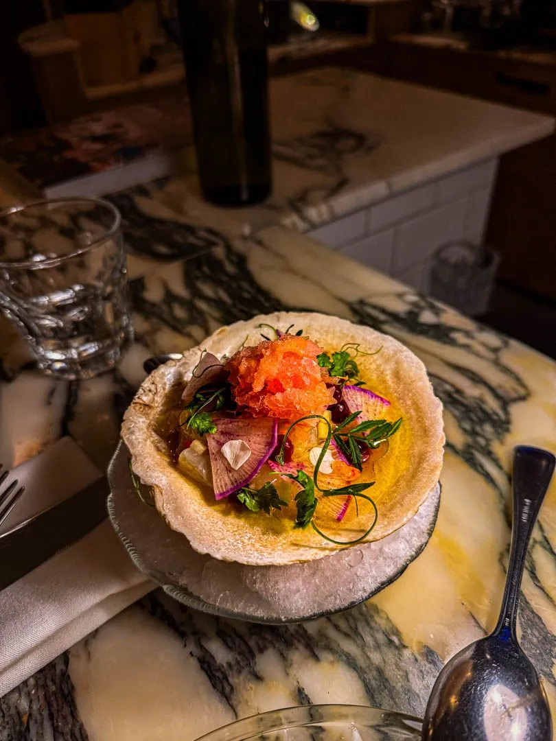 Scallop crudo with apple-grapefruit granita served in a shell on marble counter at Moccione Montreal