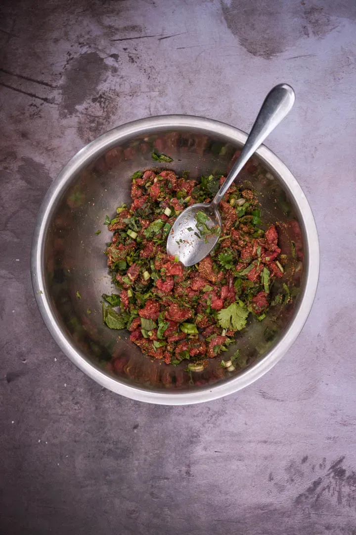 Northern Thai beef tartare plated on a wide serving dish, topped with crispy shallots and garlic chips, with fresh herb sprigs scattered on top