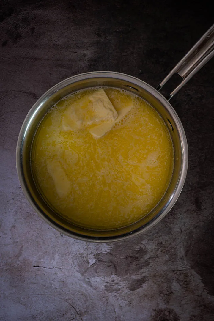 Choux dough being stirred in saucepan over heat, surface looking smooth and slightly dry