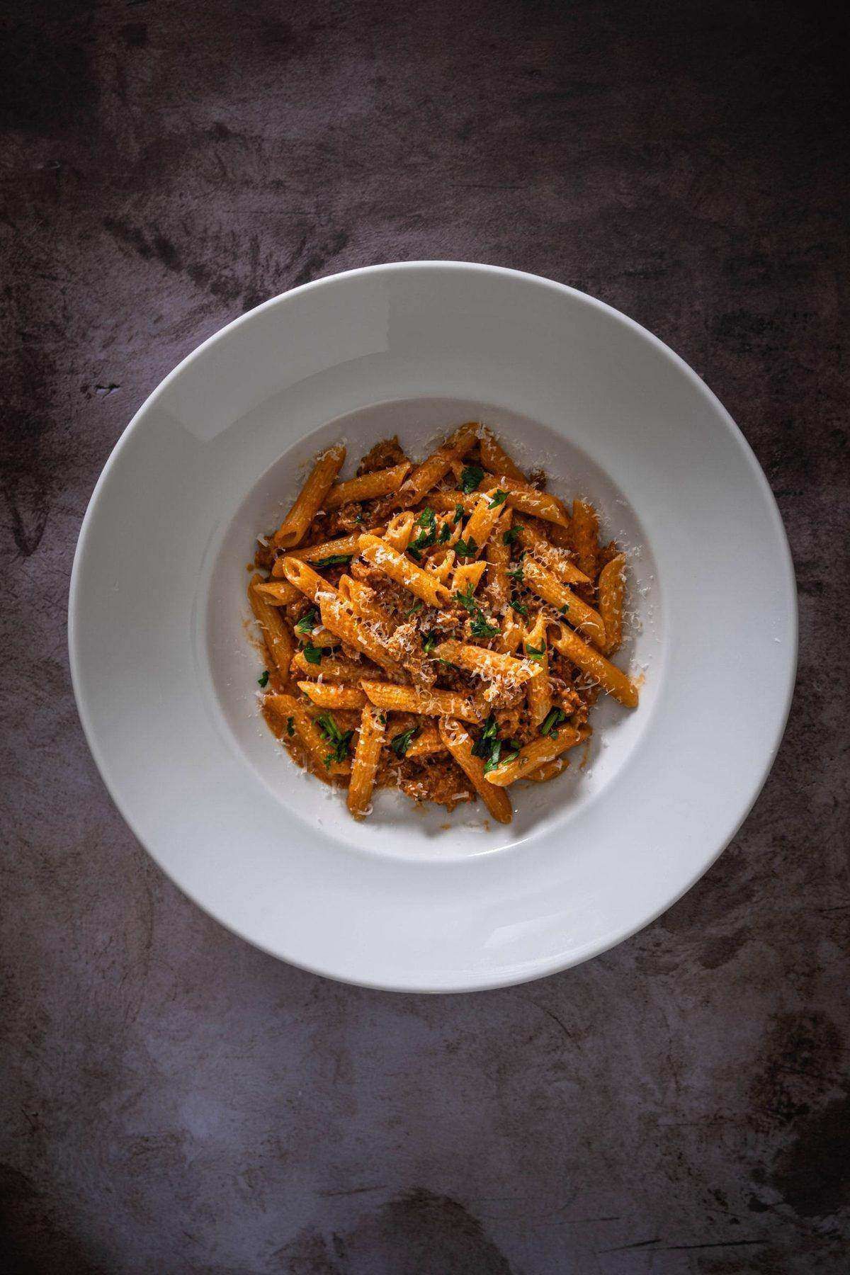 Bowl of creamy penne alla vodka with Italian sausage topped with grated Parmesan and fresh parsley