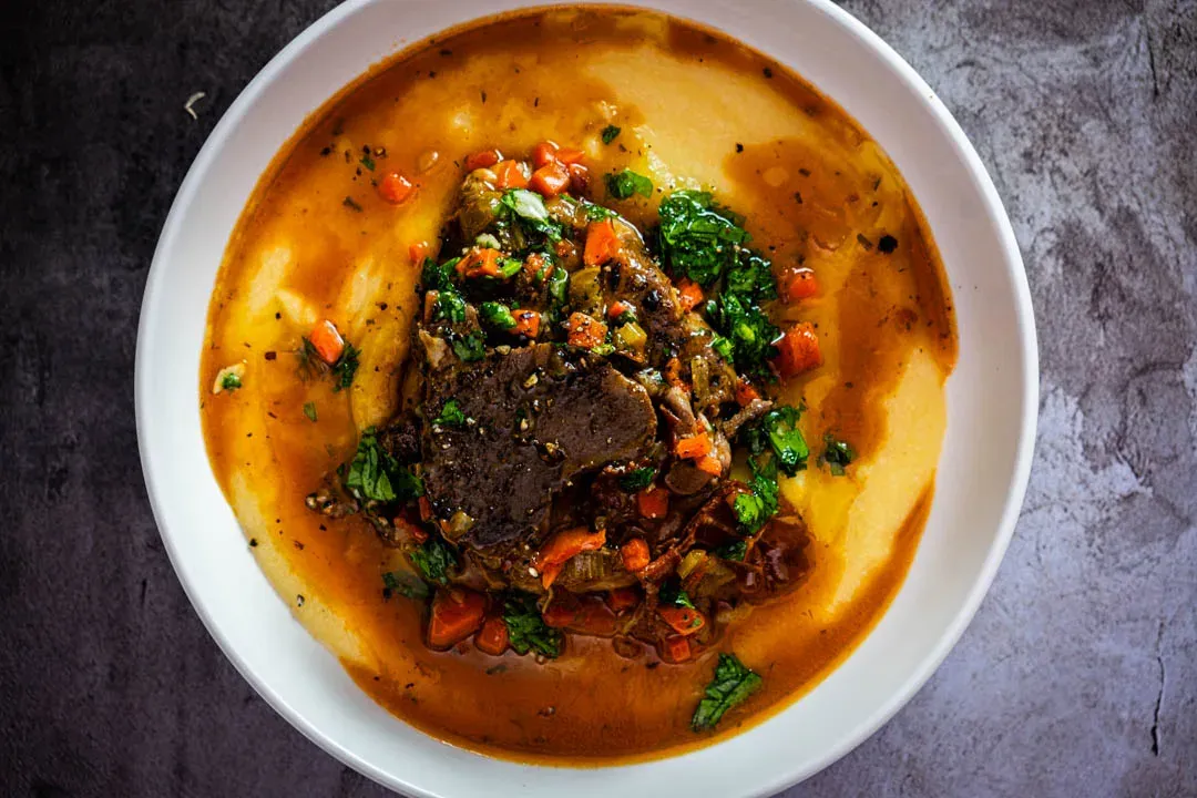 Pork osso buco with fall-apart tender braised pork shank served over creamy polenta, topped with bright green gremolata in a rustic bowl