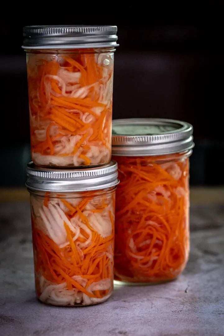 Glass mason jar filled with Vietnamese do chua pickled vegetables, showing the clear brine and colorful daikon and carrot strips