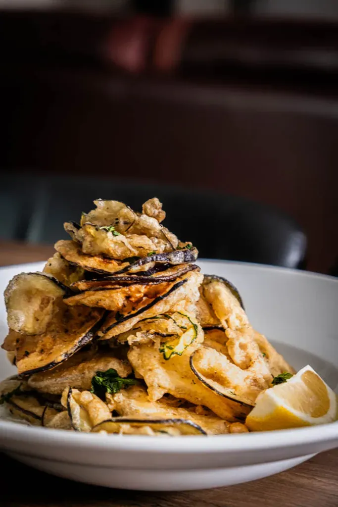 Close-up of golden crispy zucchini and eggplant chips showing the light tempura-style batter texture