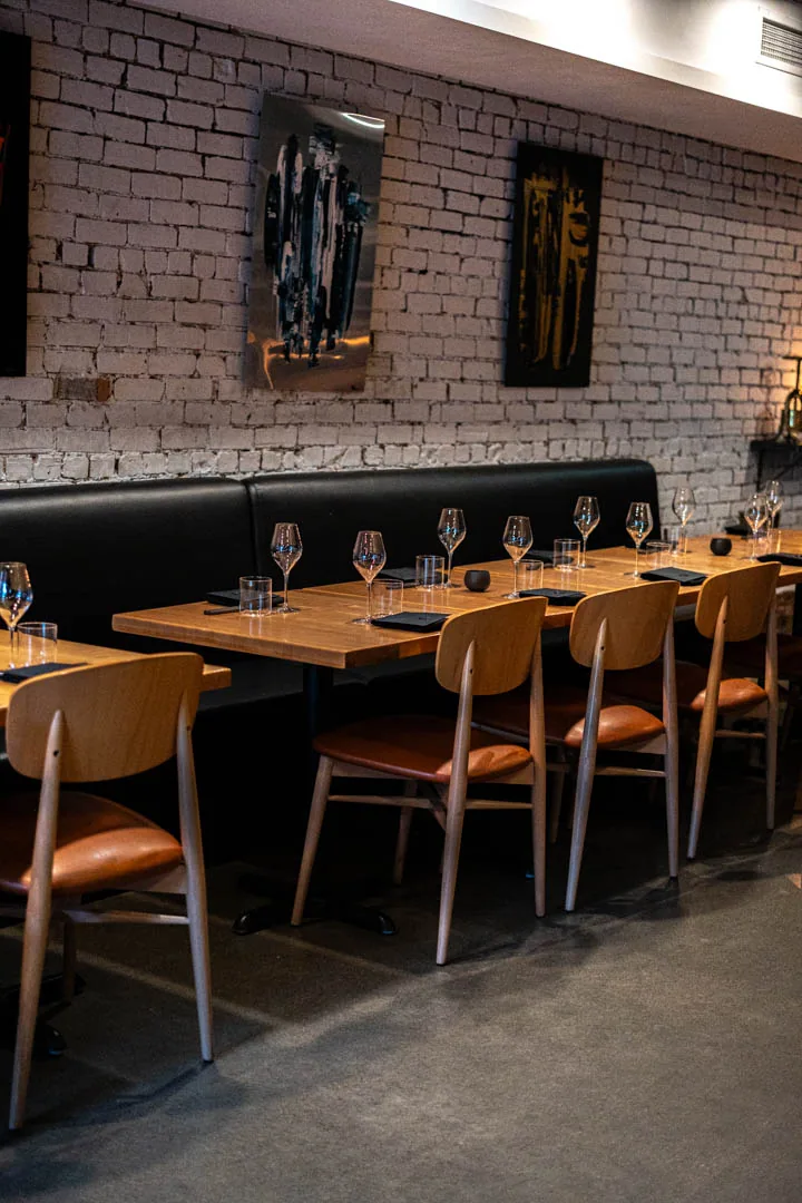 The dining room: banquette, wood tables, white brick, two dark canvases